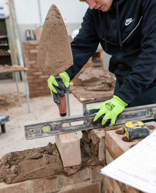 Close-up of a student in a brickwork class using a spirit level and trowel to accurately position bricks during construction practice. Close-up of a student in a brickwork class using a spirit level and trowel to accurately position bricks during construction practice.